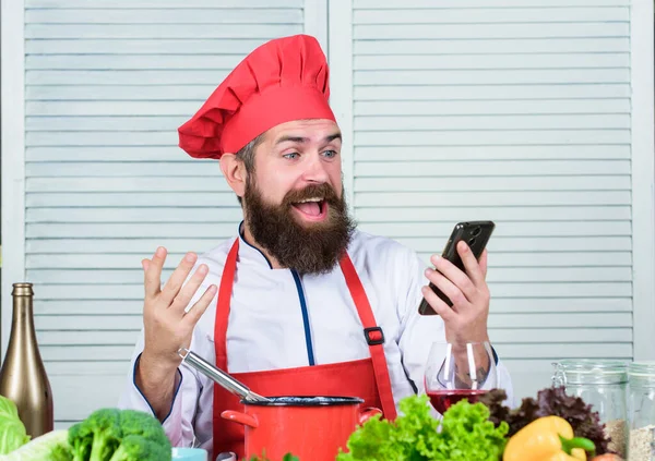 Edukacja kulinarna online. Koncepcja elearningu. Szef kuchni szuka przepis internetowy gotowanie żywności. Chef smartphone zegarek kulinarny show. Szkoła kulinarna. Hipster w kapeluszu i fartuchu uczenia się, jak gotować online — Zdjęcie stockowe