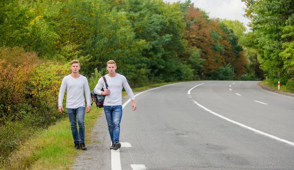 まず第一に。高速道路での旅行者ヒッチハイキング。帰り際だ。未来だ。双子が道を歩いてる。2人の兄弟が冒険に出る。友情だ。男はハイキングをする。男性カジュアルスタイル旅行付きバックパック — ストック写真