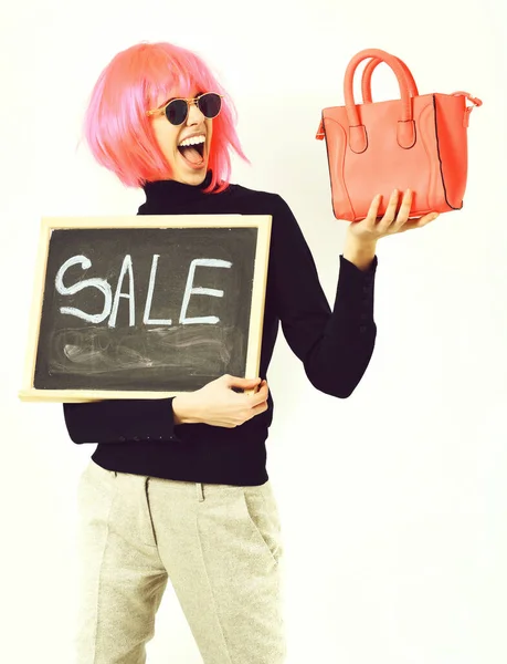 Girl in wig holding bag and board with sale inscription — Stock Photo, Image