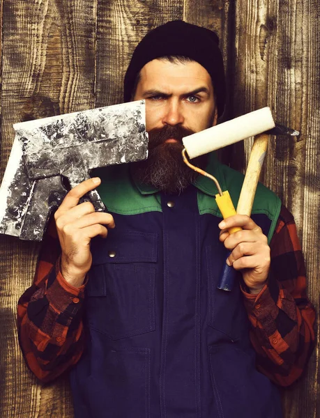Бородатый строитель держит различные строительные инструменты с серьезным лицом — стоковое фото