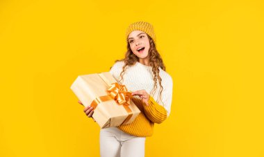 Yeni yıl beni. Elimde Noel hediyesi var. Noel konsepti. Noel hediyesi kutusu olan mutlu küçük bir kız. Çocuk hediye kutusunu sarı arka planda tutuyor. Mutlu Noeller ve yeni yıl