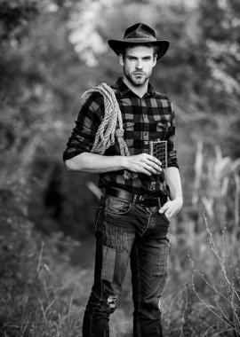 Kendine güvenen atlılar. Şapkalı adam viski içiyor. Batı kovboy açık hava portresi. Kement ipli bir kovboy. Batı. Rodeo çiftliğinde kareli gömlek. Klasik tarz adam. Vahşi Batı eski kovboy