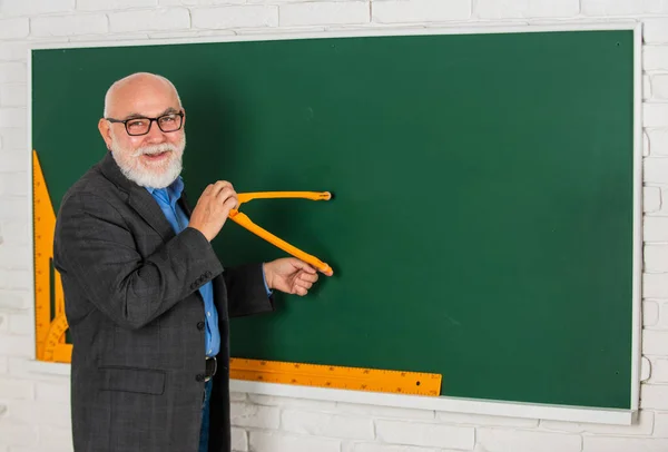 ひげを生やした家庭教師の男が黒板にコンパスで絵を描く。学校に戻って。数学のグラフィックツールの概念。知識に向かって。良い結果を得るために数学を勉強します。上級教師はコンパスツールを使う。コピースペース — ストック写真