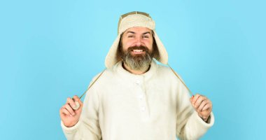 Yüz kılı konsepti. Berber servisi. Sakallı adam kulak flaplı şapka giyer. Kürklü aksesuar. Kürk giysiler. Sakallı hippi. Kış modası. Soğuk hava için sıcak şapka. Kış mevsimi için sakal bakımı