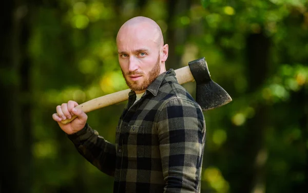 Man checkered shirt use axe. Brutal male in forest. Power and strength. Lumberjack carry ax. Bald woodsman. Harvest firewood. Hike vacation. Hike in forest. Forest care. Determination of human spirit