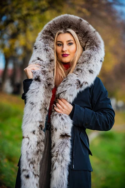 Luxe segment merk. Luxe bont. Schoonheid en mode. Vrouw draagt een jas met een grote harige kap. Valse bontstof. Elegante meidenwandeling in het herfstpark. Pelskleding. Echt warm en gezellig. Dure kleding — Stockfoto