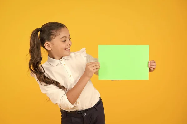 Glorieuse couleur. Petite fille tenant une feuille de papier vide sur fond jaune. Petit enfant avec un livre vert vierge pour l'affectation ou le travail de projet. Papier d'examen. Copier du papier, espace de copie — Photo