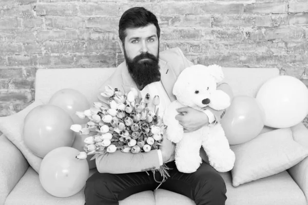 Romantic gift. Macho getting ready romantic date. Man wear blue tuxedo bow tie hold flowers bouquet. Best boyfriend ever. Romantic man with flowers and teddy bear sit on couch waiting girlfriend — Stock Photo, Image