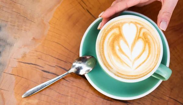 Design on surface of latte. Challenge for latte artist. Top view coffee cup on wooden table. Beautiful pattern heart created by microfoam. Coffee shop and cafe concept. Female hands cappuccino — Stock Photo, Image