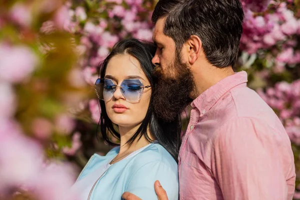 Innamorata della primavera. Amore tenero. Un paio di alberi di sakura. Tutti fiori per lei. Uomo e bella donna godendo di fiori di ciliegio rosa. Appuntamento romantico. Coppia innamorata che si coccola all'aperto. Persone di moda — Foto Stock