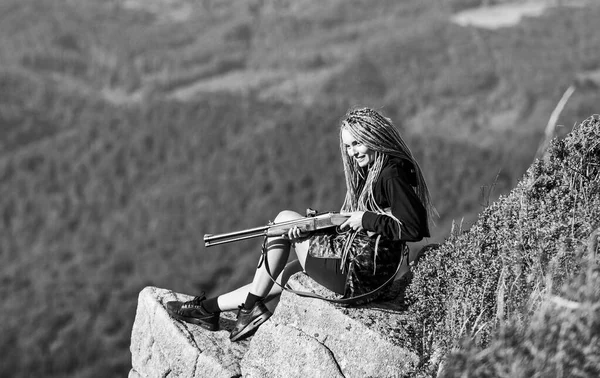 Apuntando al concepto. Chica amazónica sentarse en el acantilado preparar arma para la caza. Temporada de caza. Hunter montañas paisaje fondo. Un guerrero sexy. Mujer atractivo pelo largo cara bonita agarre rifle para la caza — Foto de Stock