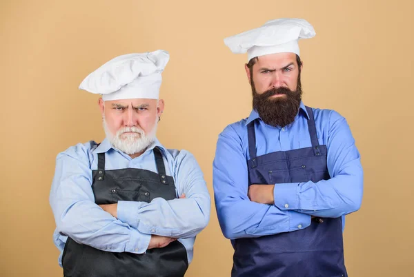 who is the best. family dinner. father and son cooking. commercial kitchen at restaurant. professional chefs. serious men in cook hat. mature bearded chef. tired of cooking. masters of kitchen