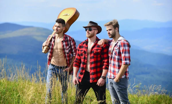 Adventurers squad. Long route. Tourists hiking concept. Hiking with friends. Men with guitar hiking on sunny day. Group of young people in checkered shirts walking together on top of mountain