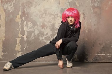 Spor elbiseli kız soyut duvarda bacak esnetiyor.