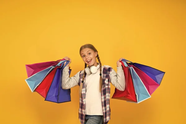 Preparación y celebración navideña. Compras y venta el viernes negro. Consumidor adicto. Sumérgete en compras. Niño feliz con bolsas de papel. Niña sonrisa con bolsas de compras sobre fondo amarillo —  Fotos de Stock