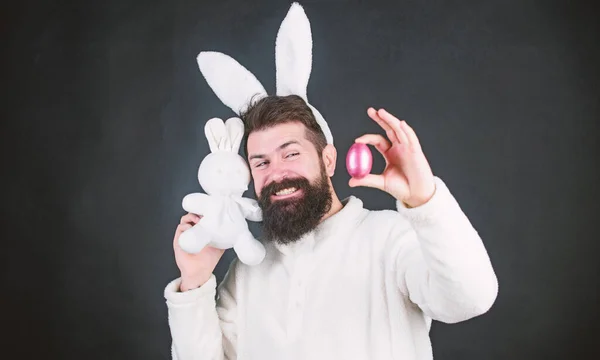 Lente, nieuw leven en vruchtbaarheid. Baard man in konijnenkostuum met paaseieren en haas speelgoed. Voorjaarsvakantie. Gelukkige man met konijnenoren met konijnenspeelgoed en ei. Moge uw Pasen ei celent zijn. — Stockfoto