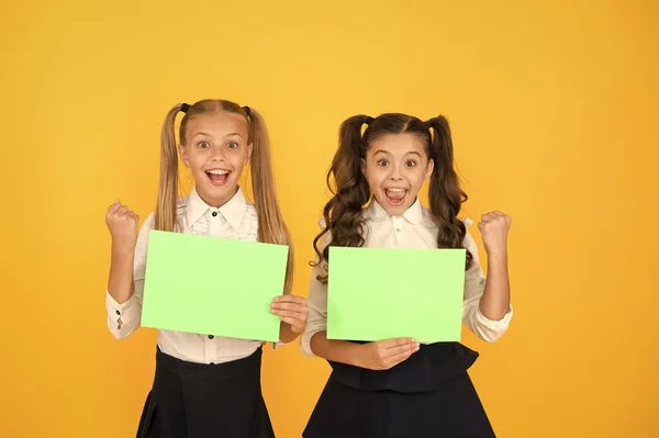 숙제 완료. 노란색 배경에 빈 숙제 시트를 들고 행복한 작은 아이들. 숙제 할당에 대한 빈 녹색 학교 포스터와 함께 미소 귀여운 어린 소녀. 숙제,복사 공간 — 스톡 사진