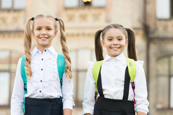 Cute schoolgirls with long ponytails looking charming. Ending of school year. Lucky to meet each other. Cheerful smart schoolgirls. Happy schoolgirls outdoors. Small schoolgirls wear school uniform — Stock Photo, Image