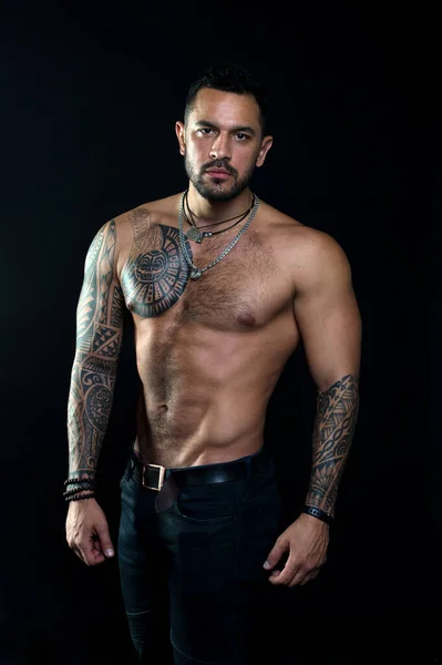 Macho sexy bare torso. Fit model with tattoo art skin. Sportsman or athlete with beard and hair. Sport and fitness. Masculinity. Muscular torso. Jewelry for real men. Bearded man with tattooed torso