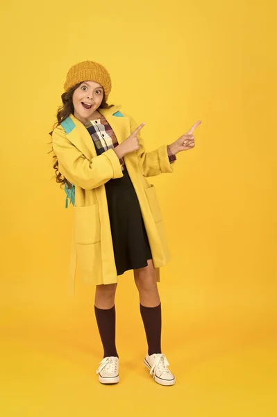 Mira atentamente. Niño sorprendido en la moda otoñal señalando algo. Pequeña colegiala con polilla abierta apuntando fondo amarillo. Usando el gesto de señalar para dirigir la atención. Señalar el producto —  Fotos de Stock