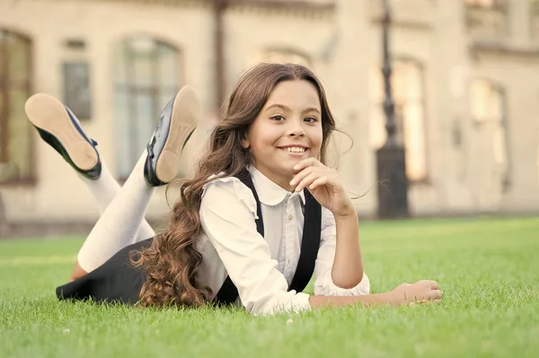 Torniamo in classe e sembriamo felici. Felice bambina rilassarsi sull'erba verde. Bambino piccolo allegro con sorriso felice e sguardo formale. Il ragazzo adorabile si diverte a scuola. Sembra felice a scuola. — Foto Stock