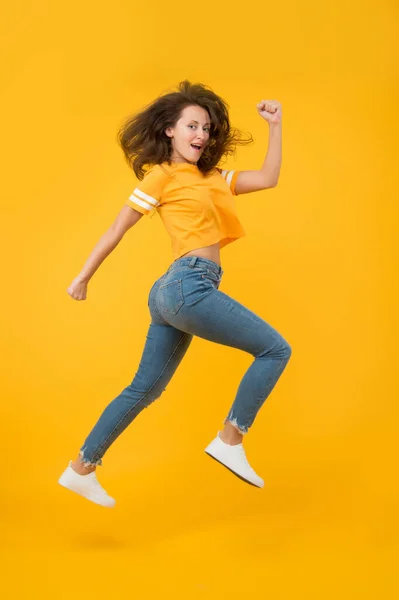 Voel innerlijke energie. Een energieke vrouw die rent of springt. Skinny jeans staat haar goed. Sexy meisje gele achtergrond. Sensueel meisje in casual stijl. Mooi meisje met lang haar. Modestijl. Schoonheid en make-up — Stockfoto