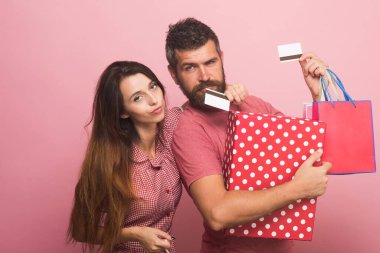 Çift, pembe arka planda büyük bir kutu ve alışveriş torbası tutuyor.