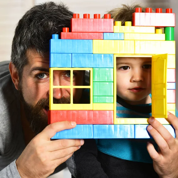 Padre e hijo con caras tranquilas detrás de ladrillos coloridos construcción — Foto de Stock