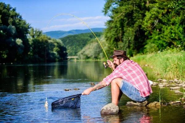 Pesca hipster com colher-isca. pescador bem sucedido na água do lago. mosca peixe passatempo do homem. Hipster em camisa quadriculada. pesca grande jogo. relaxar na natureza. Belo dia para pescar. homem com peixe na vara — Fotografia de Stock