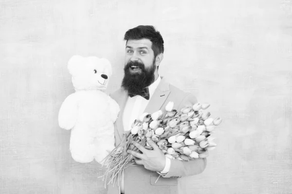 Happy and in love. Gentleman making romantic surprise for her. Gentleman romantic gift. Birthday greetings. Happy birthday my love. Man bearded gentleman suit bow tie hold teddy bear and bouquet — Stock Photo, Image