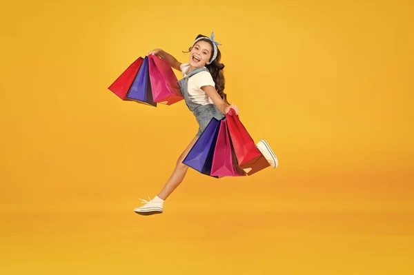 Inspiring shopping. Trends and brands. Towards discounts. Happy girl jump with shopping bags. Little child smile with paper bags. Holidays preparation and celebration. Shopping on black friday — Stock Photo, Image