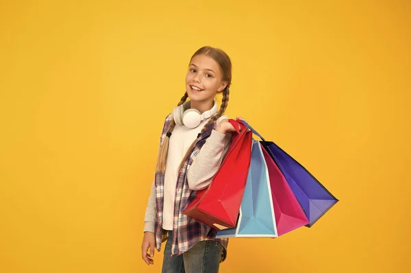 買い物に飛び込む。紙袋を持った幸せな子供。黄色の背景にショッピングバッグと女の子の笑顔。休日の準備とお祝い。ブラック・フライデーでの買い物と販売。献身的な消費者 — ストック写真