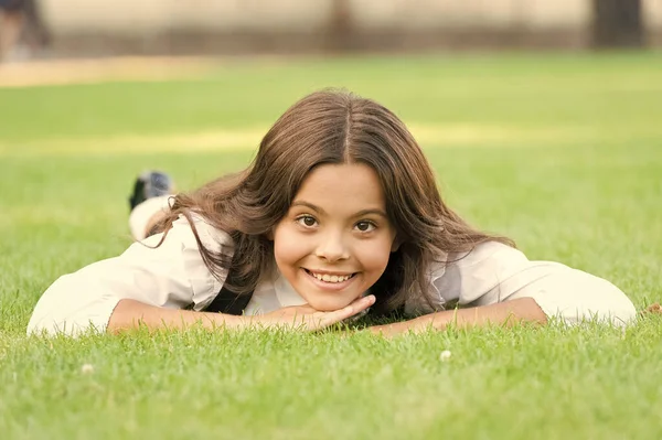 Keep calm and relax. Happy child with school look lying on green grass. Little girl smile with formal fashion look. Beauty look of small schoolchild — Stock Photo, Image