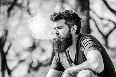 Uzun sakallı adam sigara içmekten rahatlamış. Sakallı ve bıyıklı adam duman üflüyor. Beyaz aromalı duman bulutları. Stres atma konsepti. Tüttüren sakallı adam. Elektronik sigara içiyorum.