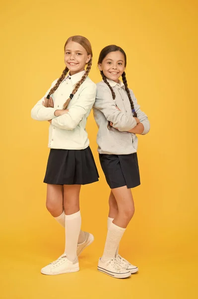Together since school. education. back to school. kid fashion. Friendship and sisterhood. happy girls in school uniform. smart little girls on yellow background. knowledge day. childhood happiness — Stock Photo, Image