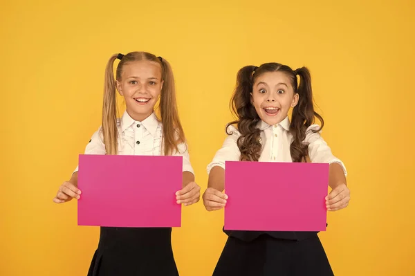 Promover con publicidad. Niños pequeños y felices mostrando hojas de papel rosa para publicidad sobre fondo amarillo. Pequeña niña publicidad producto o evento. Publicidad y marketing, espacio para copias — Foto de Stock