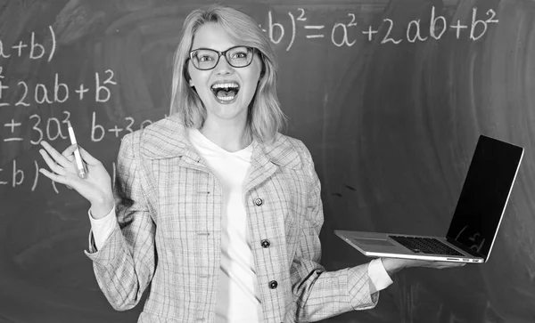 Woman teacher wear eyeglasses holds laptop surfing internet. Digital technologies concept. Educator cheerful lady with modern laptop surfing internet chalkboard background. Education is fun Royalty Free Stock Photos