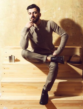 Sakallı adam merdivenlerde oturuyor, ciddi bir yüzü var.