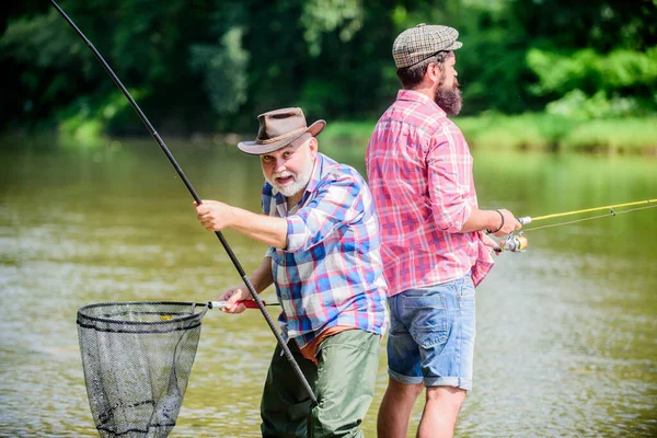 Känn på växeln. far och son fiskar. hobby- och idrottsverksamhet. Öring bete. Sommarhelgen. mogna män fiskare. två glada fiskare med fiskespö och nät. manlig vänskap. Familjeband — Stockfoto