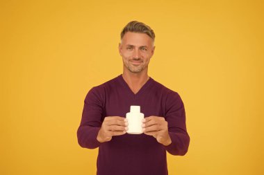 Heyecan verici erkek parfümü. Mutlu adam parfüm şişesini sarı arka planda tutuyor. Parfüm sunan yakışıklı bir adam. Eau de Tuvalet. Kozmetik ürünü. Kozmetik. Parfüm reklamı. Parfüm markası, boşluğu kopyala