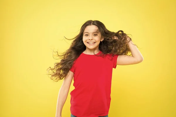 強い持続的な風は、波状と巻き毛の長い髪にもつれやスナッグを作成することができます。髪を傷つける事女の子愛らしい子供長い波状の髪黄色の背景。風はまた、髪を損傷することができます — ストック写真