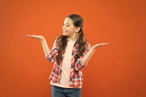 Guess what. small girl checkered shirt. happy child. childrens day. childhood memory. little girl orange background. kid fashion. smiling school girl. worker uniform. kid long hair presenting product. — Stock Photo, Image