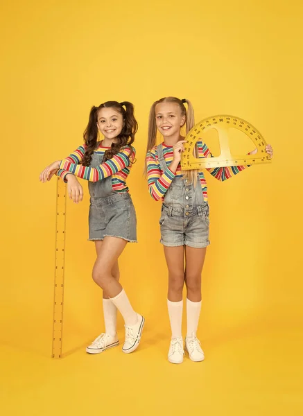 Interesting task. School club. School children with measuring instruments. Little girls ready geometry lesson. Cute schoolgirls holding protractor and ruler for school lesson. Studying measurement