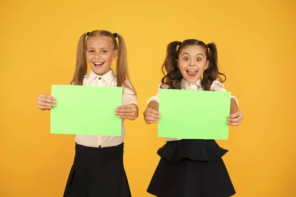 Reclame-idee voor school. Gelukkige meisjes die papier vellen voor een bepaald idee op gele achtergrond. Kleine schattige kinderen glimlachen van Genius idee. Kleine kinderen met leeg papier voor uw idee, kopieer ruimte — Stockfoto