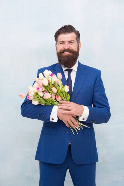 Man with bouquet tulips. prepare for mothers day holiday. flower surprise for her. bearded man in formal suit greeting. happy valentines day. womens day gift tulips. spring flowers