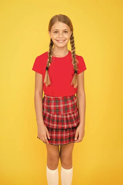 Bonitinho adorável. Menina bonito encantador sorriso no fundo amarelo. Menina pequena feliz vestindo roupas vermelhas. Menina com tranças longas de cabelo trançado. Menina adorável orgulhoso de ser aluno. Infância feliz — Fotografia de Stock