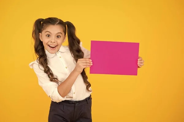 학교는 행복 한 곳입니다. 노란 배경에 빈 분홍색 종이를 들고 있는 행복 한 어린이. 어린 소녀는 빈 포스터로 행복하게 웃습니다. 널 행복하게 해 줄 거야 복사하는 공간 — 스톡 사진
