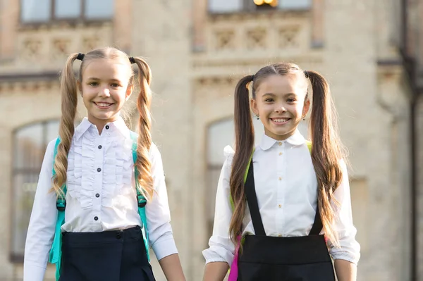 Einde schooljaar. Gelukkig hebben we elkaar ontmoet. Vrolijke slimme schoolmeisjes. Gelukkige schoolmeisjes buiten. Kleine schoolmeisjes dragen schooluniform. Leuke schoolmeisjes met lange paardenstaarten op zoek charmant — Stockfoto