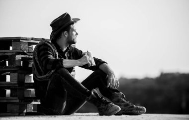 Çiftçi alkol içerken çiftliğinden manzaranın keyfini çıkarır. Gün batımını izliyorum. Çiftçi kovboy yakışıklı adam çiftlikte sıkı çalıştıktan sonra dinleniyor. Romantizm batı kültürü. Şapkalı çiftçi rahatına bak. Akşam vakti.