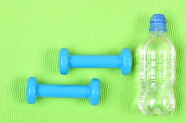 Yeşil dalgalı arkaplanda siyan plastikten yapılmış dambıllar.